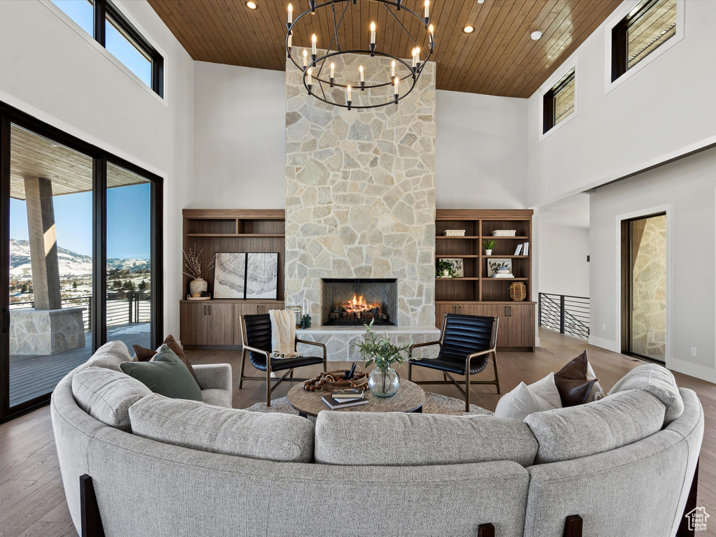 Living room with a towering ceiling, a stone fireplace, wood finished floors, wooden ceiling, and baseboards