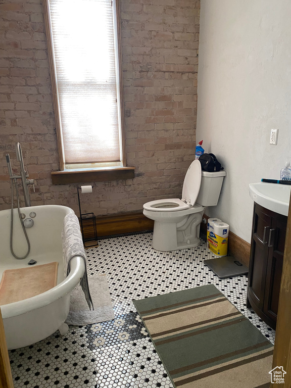 Full bath with a freestanding tub, baseboards, toilet, and brick wall