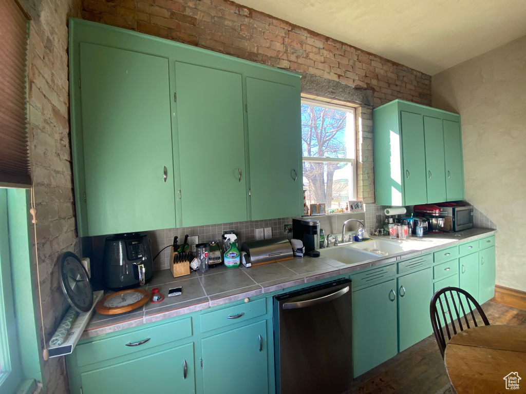 Kitchen featuring tile countertops, stainless steel dishwasher, a sink, and tasteful backsplash