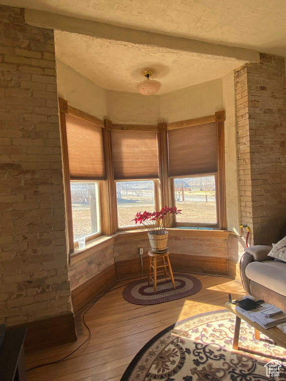 Living area featuring a textured ceiling, brick wall, hardwood / wood-style floors, and beam ceiling