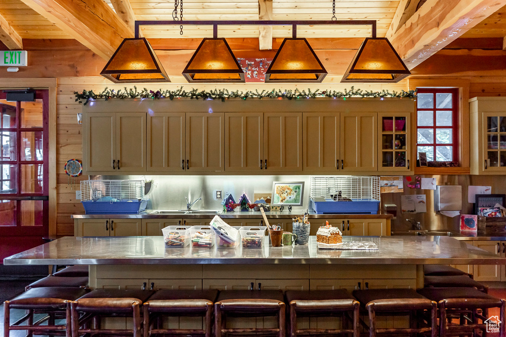 Kitchen featuring beamed ceiling, a kitchen bar, wood walls, wood ceiling, and stainless steel countertops