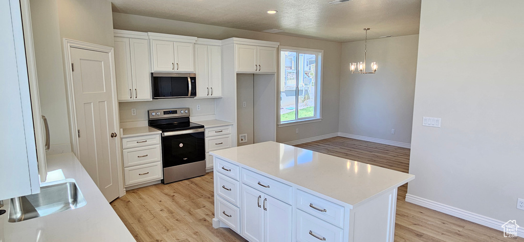 Kitchen featuring a notable chandelier, appliances with stainless steel finishes, light countertops, light wood-style flooring, and white cabinetry