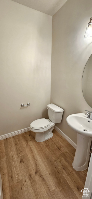 Half bath with toilet, baseboards, a sink, and wood finished floors