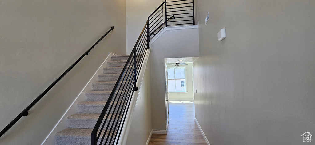 Staircase with baseboards, ceiling fan, wood finished floors, and a towering ceiling
