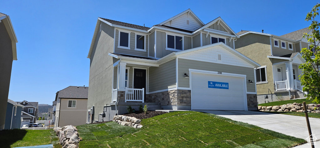 Craftsman-style home with a garage, a front yard, stone siding, concrete driveway, and a residential view
