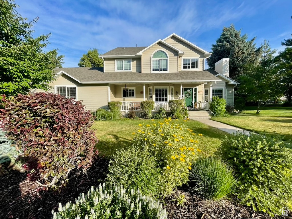 View of front facade featuring a front yard, a porch, a chimney, and a shingled roof