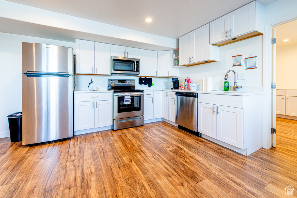 Kitchen with stainless steel appliances, light countertops, a sink, and light wood-style flooring