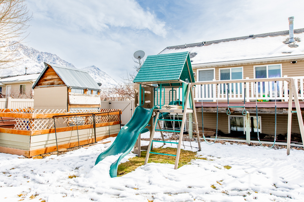 Snow covered playground featuring a playground and fence