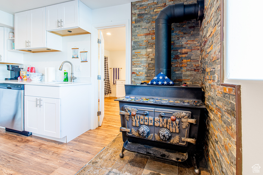 Interior details with a sink, white cabinetry, stainless steel dishwasher, light wood-type flooring, and a wood stove