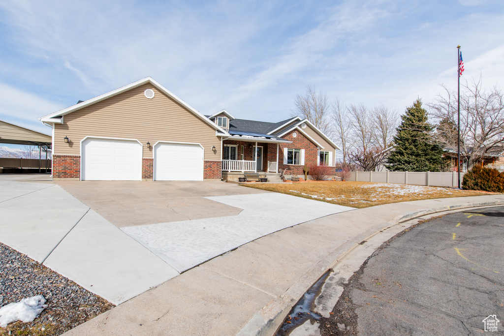 View of front facade featuring driveway, fence, a porch, and brick siding