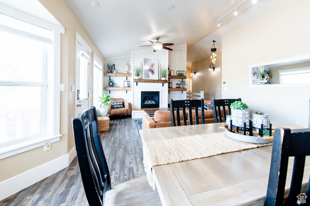 Dining area with plenty of natural light, a large fireplace, vaulted ceiling, and wood finished floors