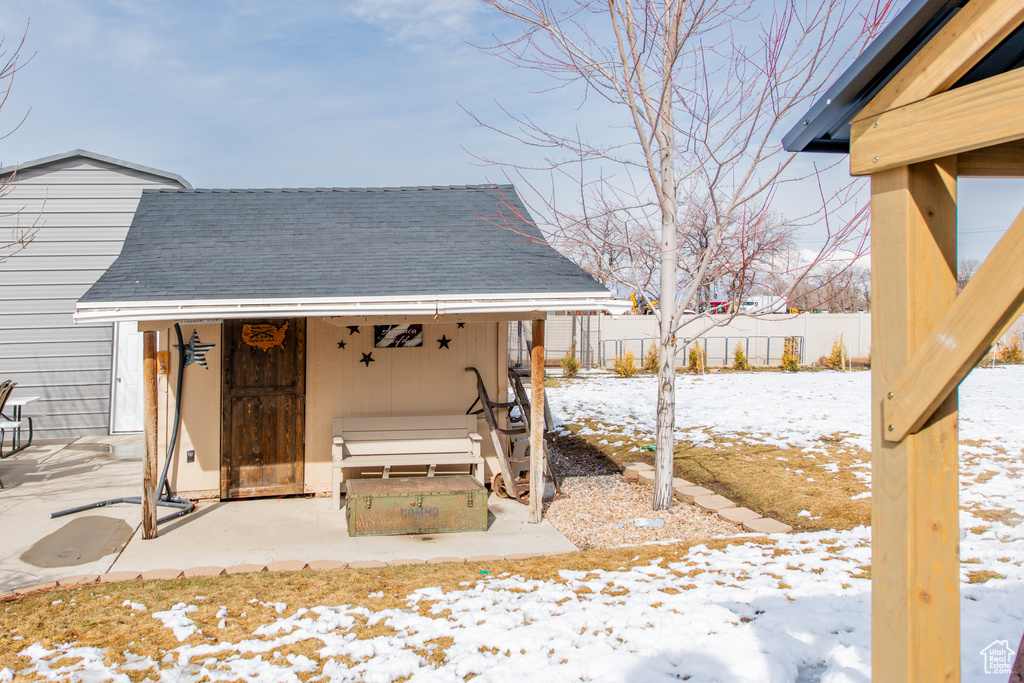 Snow covered patio featuring an outbuilding and fence