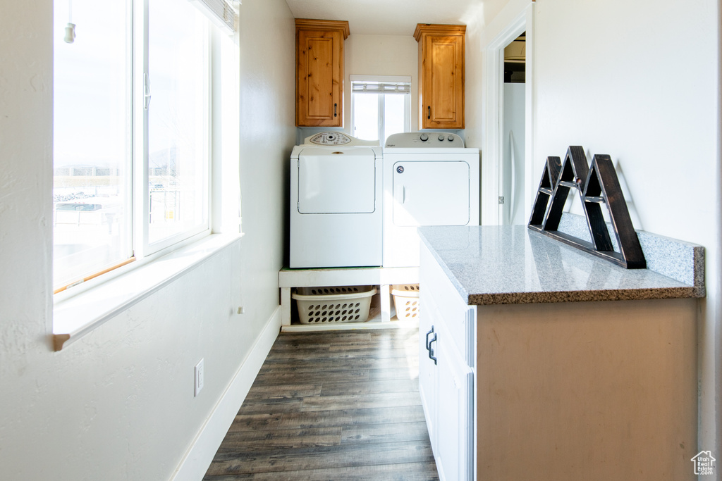 Clothes washing area featuring dark wood-type flooring, washer and dryer, cabinet space, and baseboards