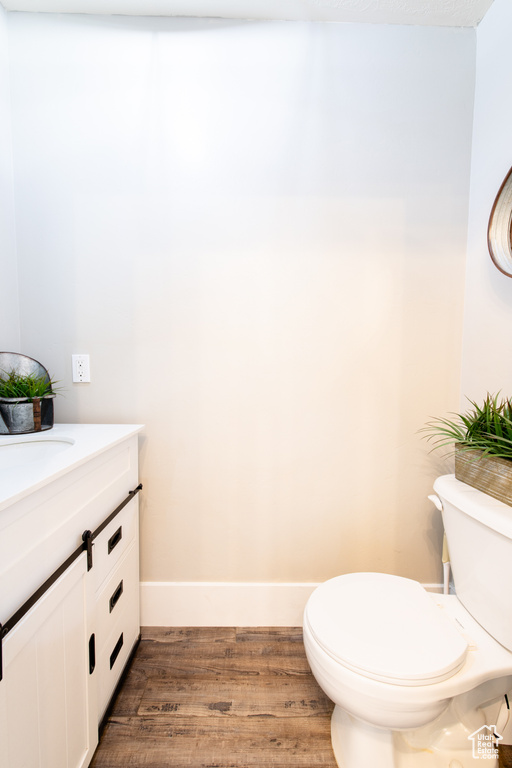 Half bathroom featuring vanity, wood finished floors, toilet, and baseboards