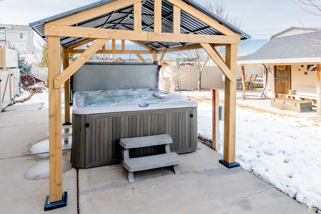 Snow covered patio featuring fence, a hot tub, and a gazebo