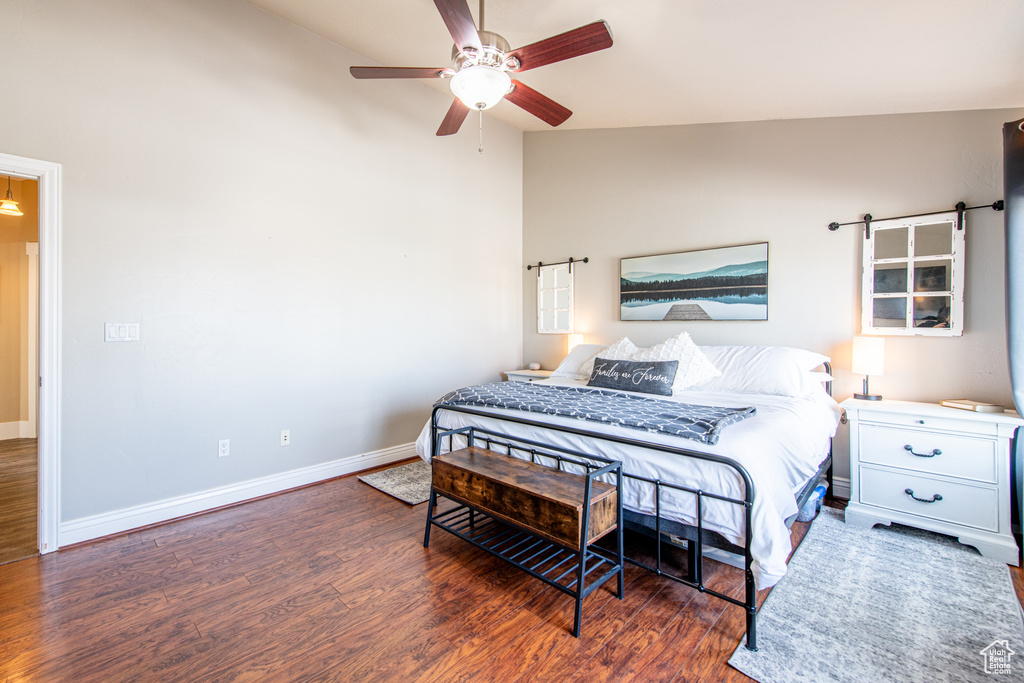 Bedroom featuring a barn door, wood finished floors, a ceiling fan, baseboards, and vaulted ceiling