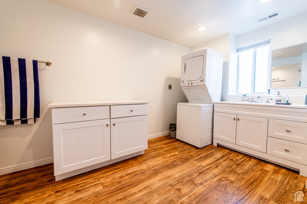 Laundry room with stacked washer and clothes dryer, visible vents, baseboards, and light wood finished floors