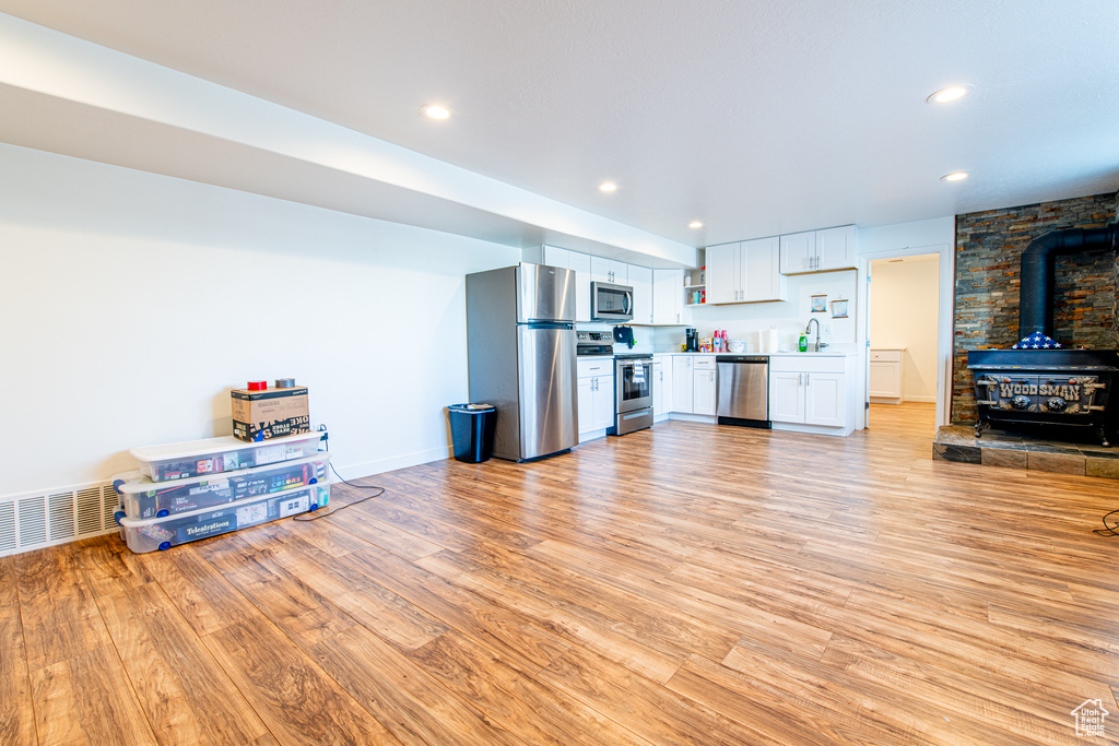 Kitchen with visible vents, white cabinets, a wood stove, stainless steel appliances, and light wood-style floors