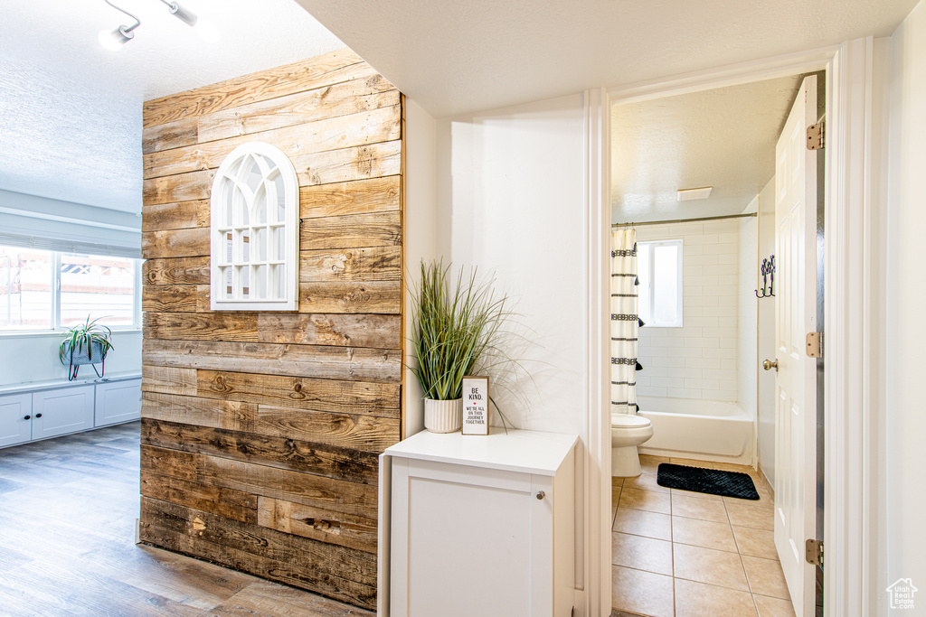 Bathroom with shower / bathtub combination with curtain, toilet, wood walls, a textured ceiling, and tile patterned floors