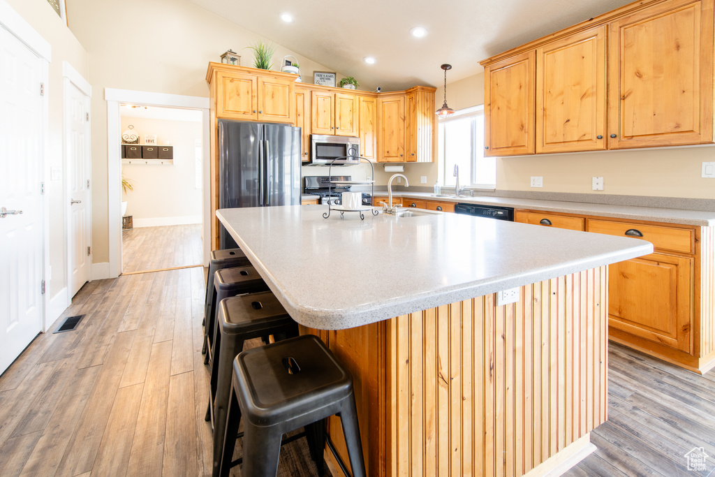 Kitchen with stainless steel appliances, lofted ceiling, visible vents, light wood-style flooring, and a sink