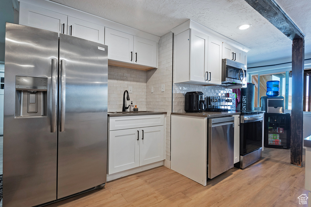 Kitchen featuring stainless steel appliances, light wood finished floors, dark countertops, and a sink