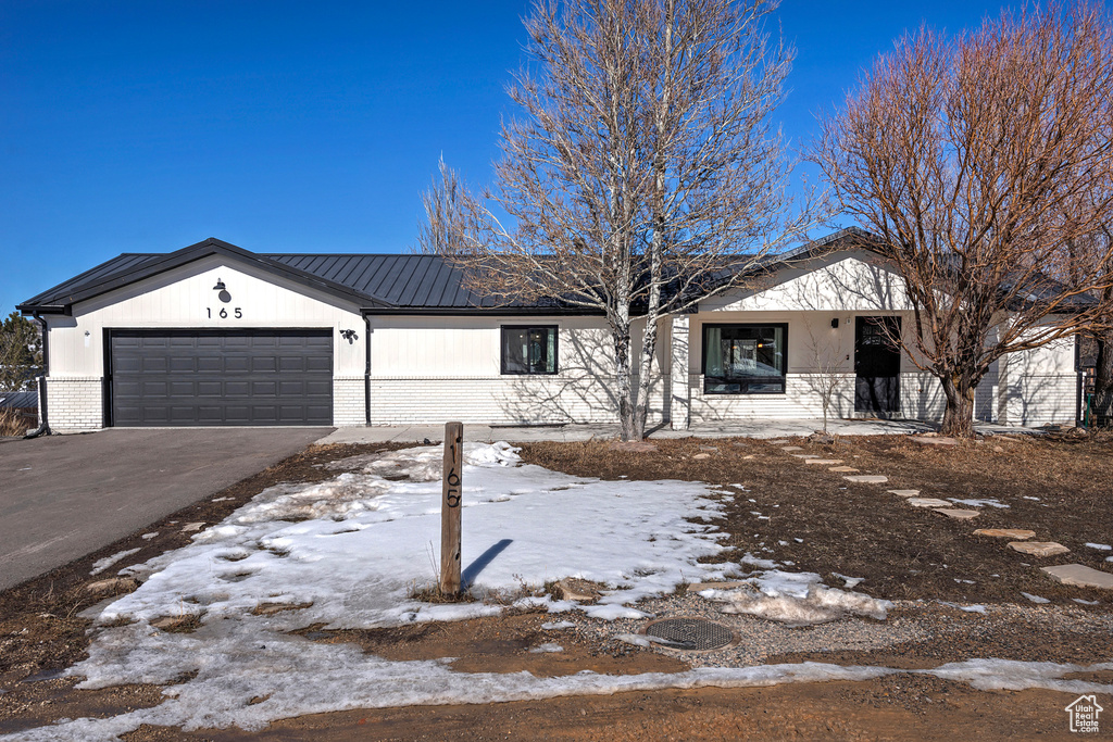 Ranch-style home with an attached garage, aphalt driveway, metal roof, and brick siding
