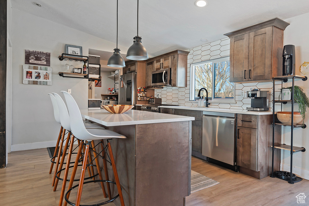 Kitchen featuring light wood finished floors, light countertops, backsplash, appliances with stainless steel finishes, and a kitchen breakfast bar
