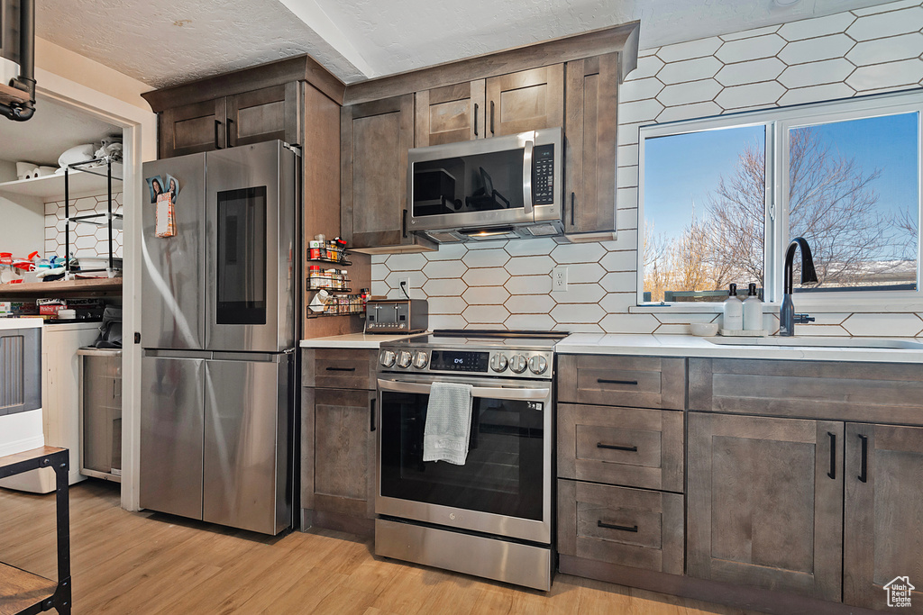 Kitchen with stainless steel appliances, a sink, light countertops, decorative backsplash, and light wood finished floors