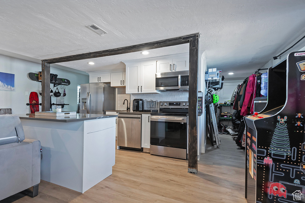 Kitchen with light wood finished floors, tasteful backsplash, white cabinets, appliances with stainless steel finishes, and a textured ceiling