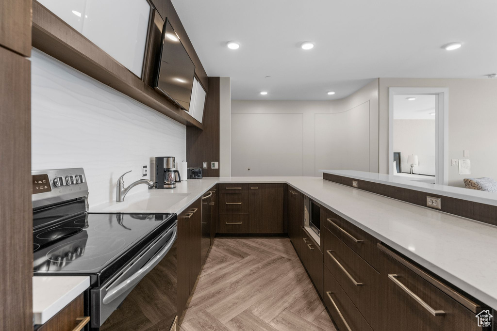 Kitchen with electric range, modern cabinets, light countertops, and dark brown cabinets