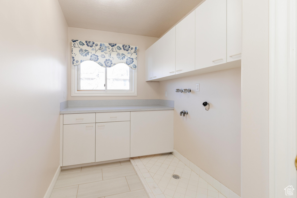 Laundry room with cabinet space, baseboards, and light tile patterned flooring