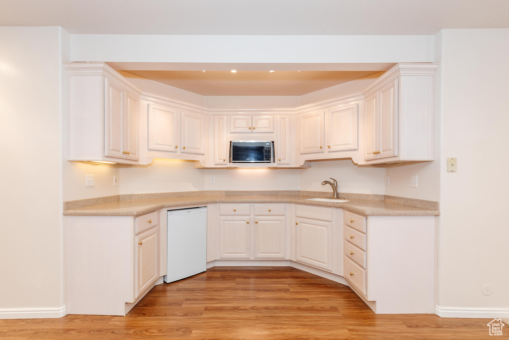 Kitchen featuring dishwasher, stainless steel microwave, light wood-style floors, and a sink