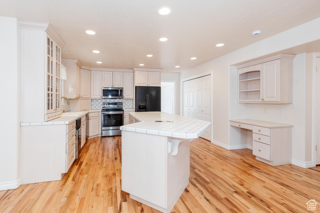 Kitchen with built in desk, stainless steel appliances, tile counters, tasteful backsplash, and a kitchen island