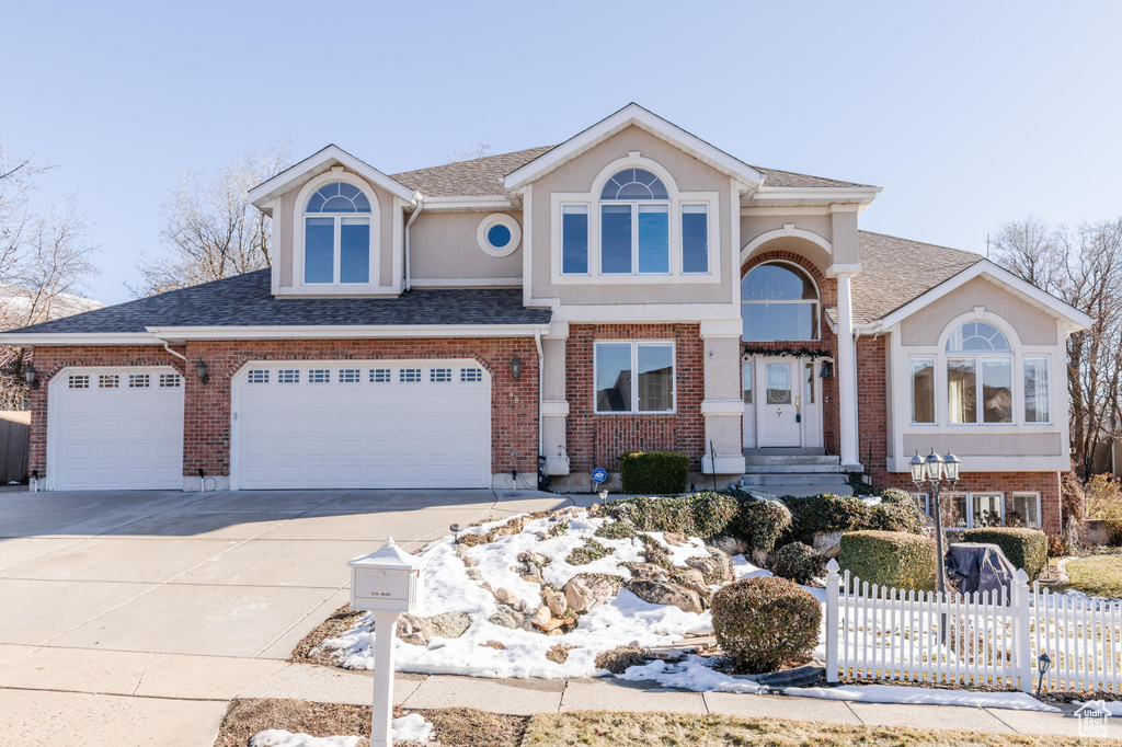 View of front of home featuring concrete driveway, brick siding, and fence