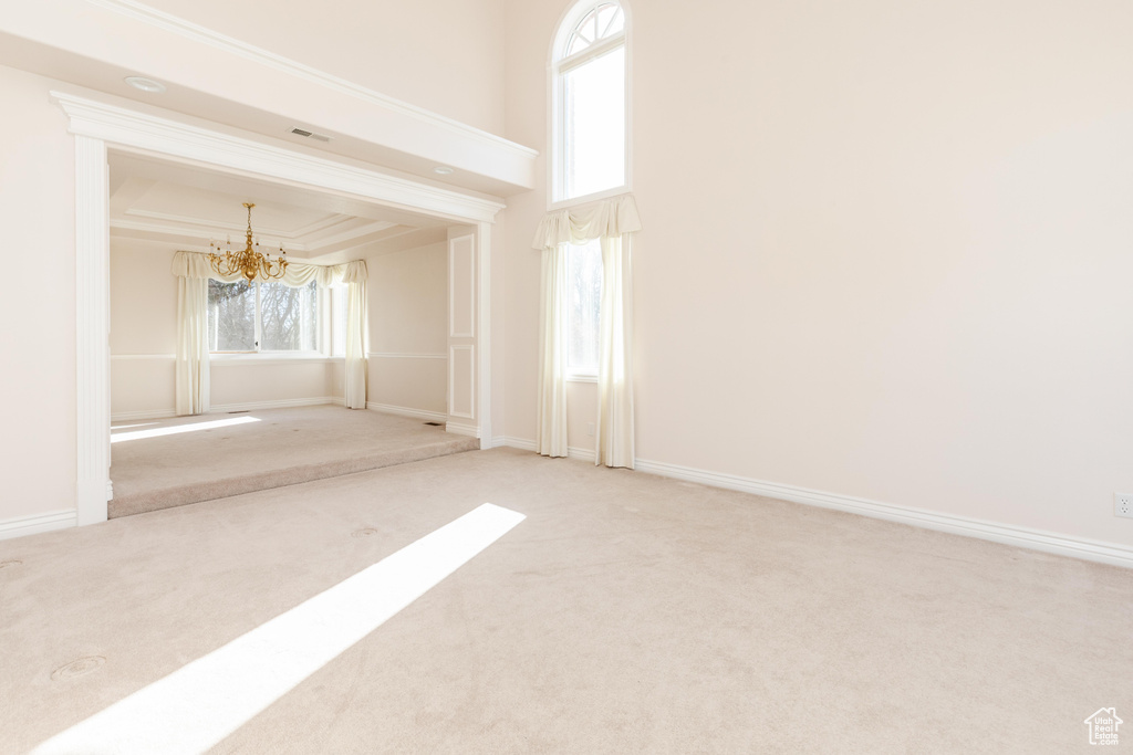 Carpeted empty room with baseboards, visible vents, an inviting chandelier, a tray ceiling, and crown molding