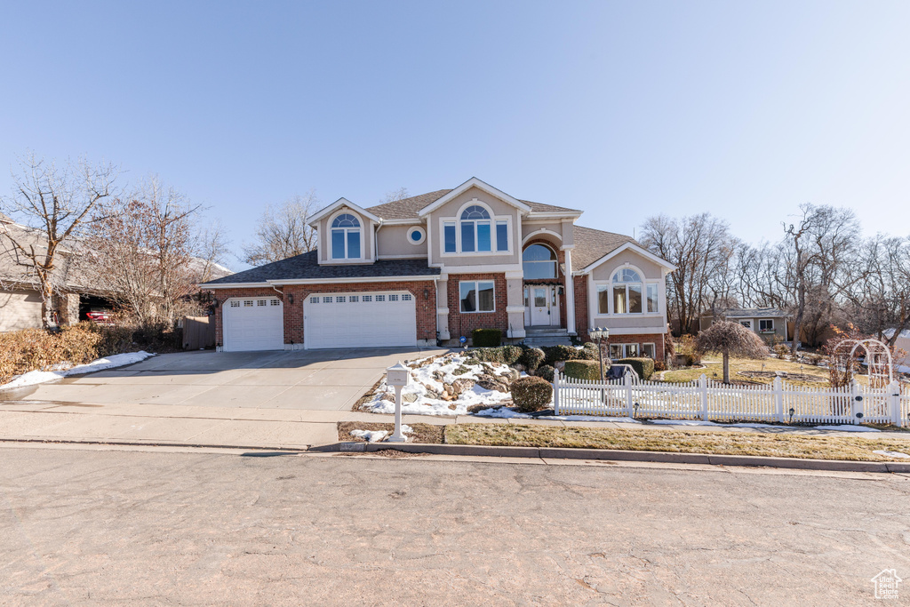 View of front facade featuring concrete driveway, roof with shingles, an attached garage, fence, and brick siding