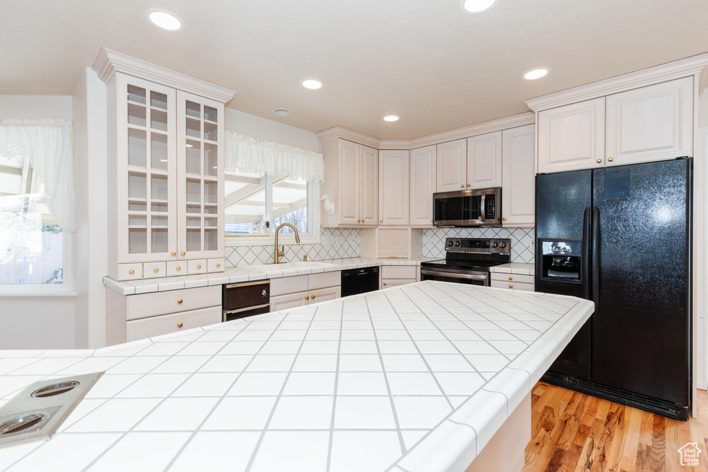 Kitchen with light wood-type flooring, black appliances, tile counters, and backsplash