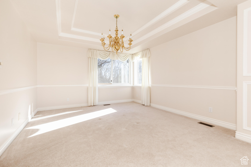 Carpeted empty room featuring visible vents, a tray ceiling, a chandelier, and baseboards