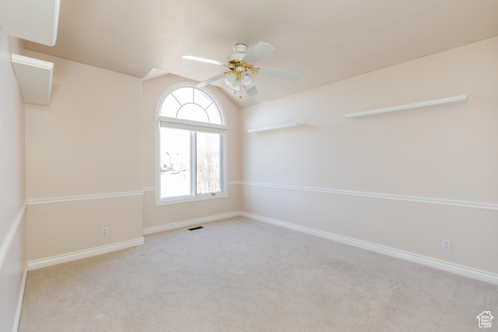 Carpeted empty room featuring lofted ceiling, ceiling fan, and baseboards