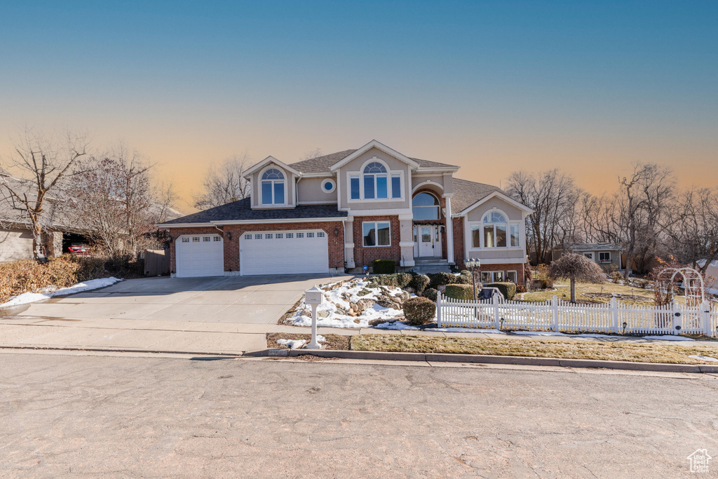 View of front of property featuring driveway, brick siding, and fence