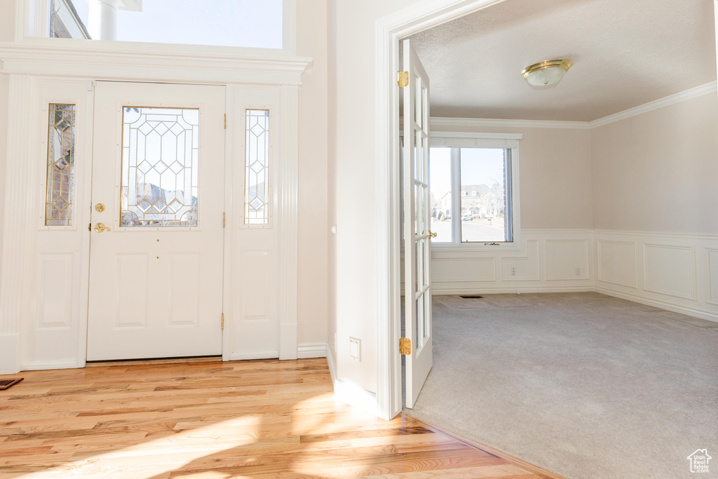 Foyer featuring a decorative wall, a wainscoted wall, visible vents, ornamental molding, and light wood-type flooring