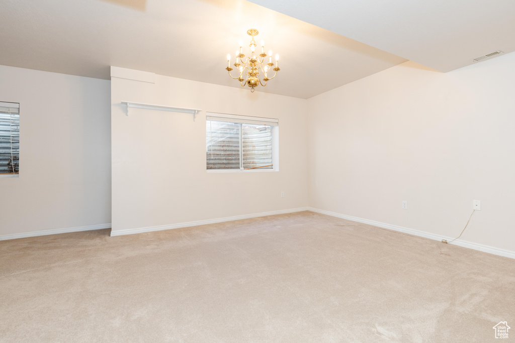 Unfurnished room with light colored carpet, visible vents, and an inviting chandelier