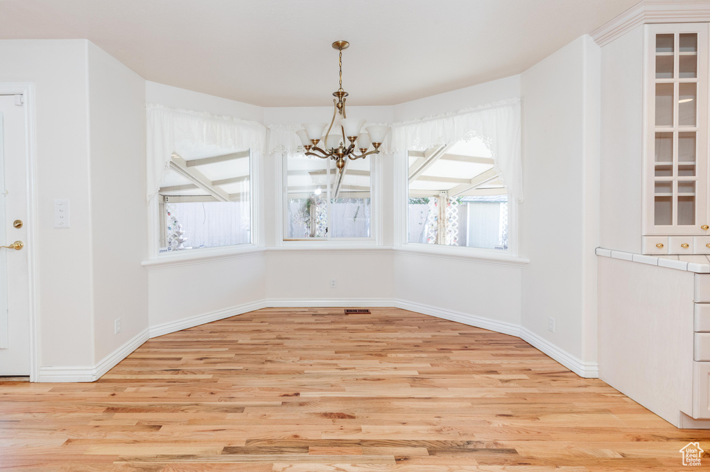 Unfurnished dining area with light wood-type flooring, a notable chandelier, and baseboards