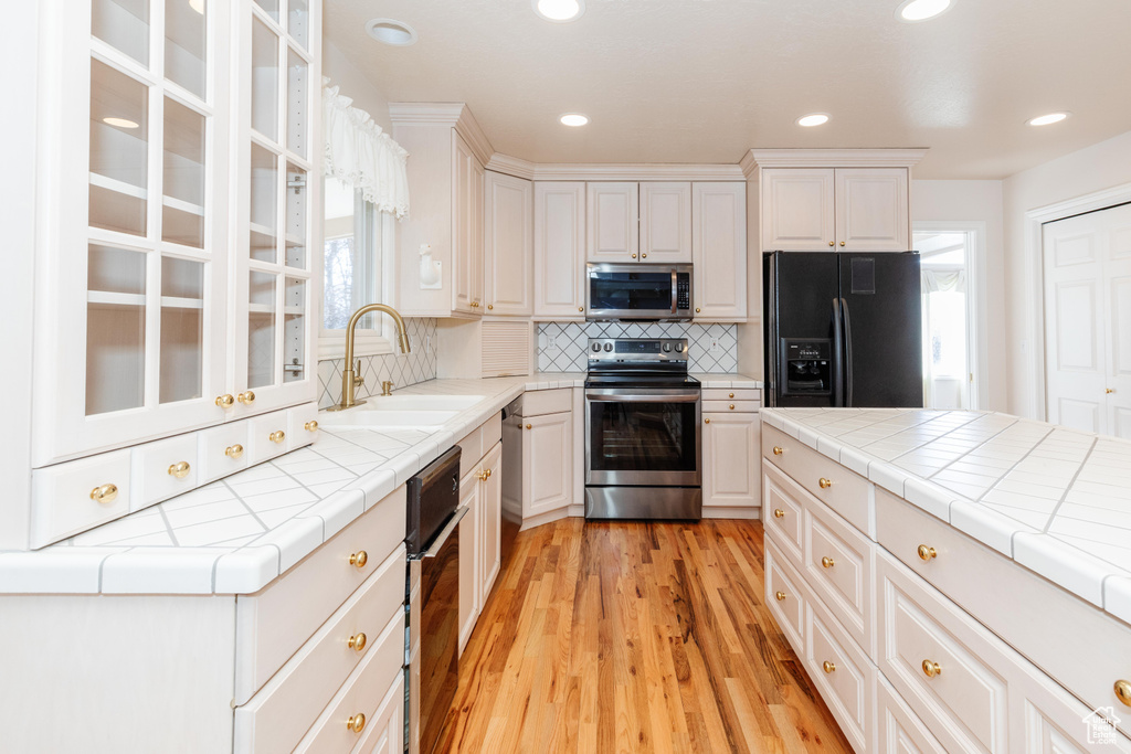 Kitchen with white cabinets, light wood-style flooring, a sink, stainless steel appliances, and backsplash