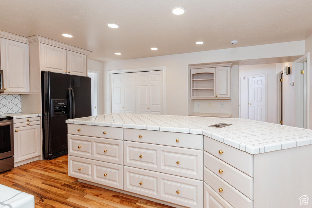 Kitchen with recessed lighting, black fridge, stainless steel electric range, backsplash, and light wood finished floors