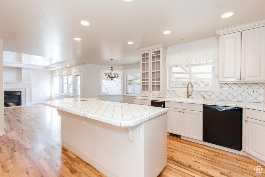 Kitchen with tile counters, light wood-style flooring, decorative backsplash, open floor plan, and dishwasher