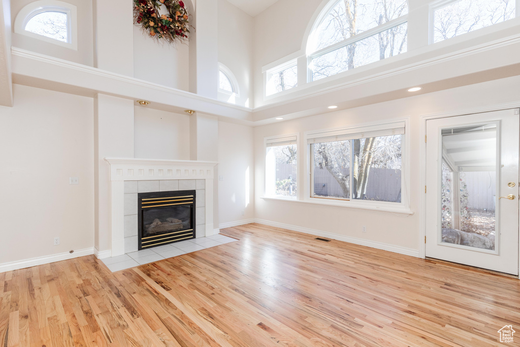 Unfurnished living room with a high ceiling, a fireplace, baseboards, and wood finished floors