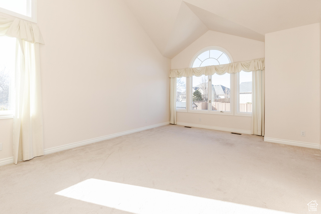 Carpeted spare room featuring visible vents, vaulted ceiling, and baseboards