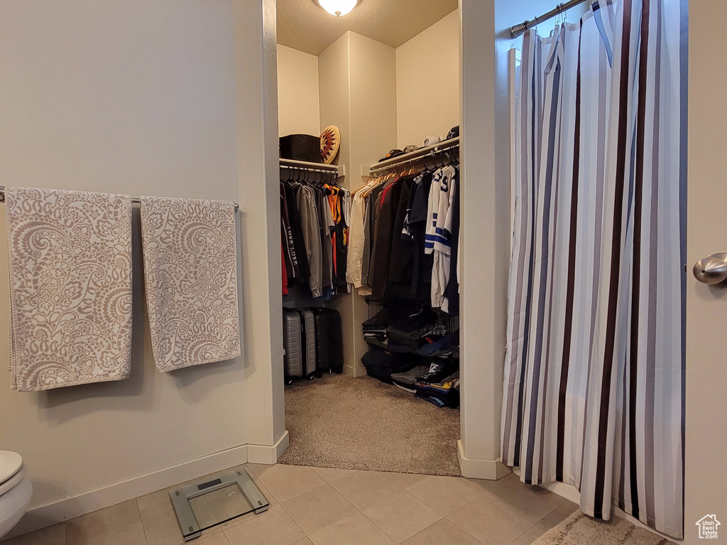 Bathroom with toilet, a shower with shower curtain, baseboards, tile patterned floors, and a walk in closet