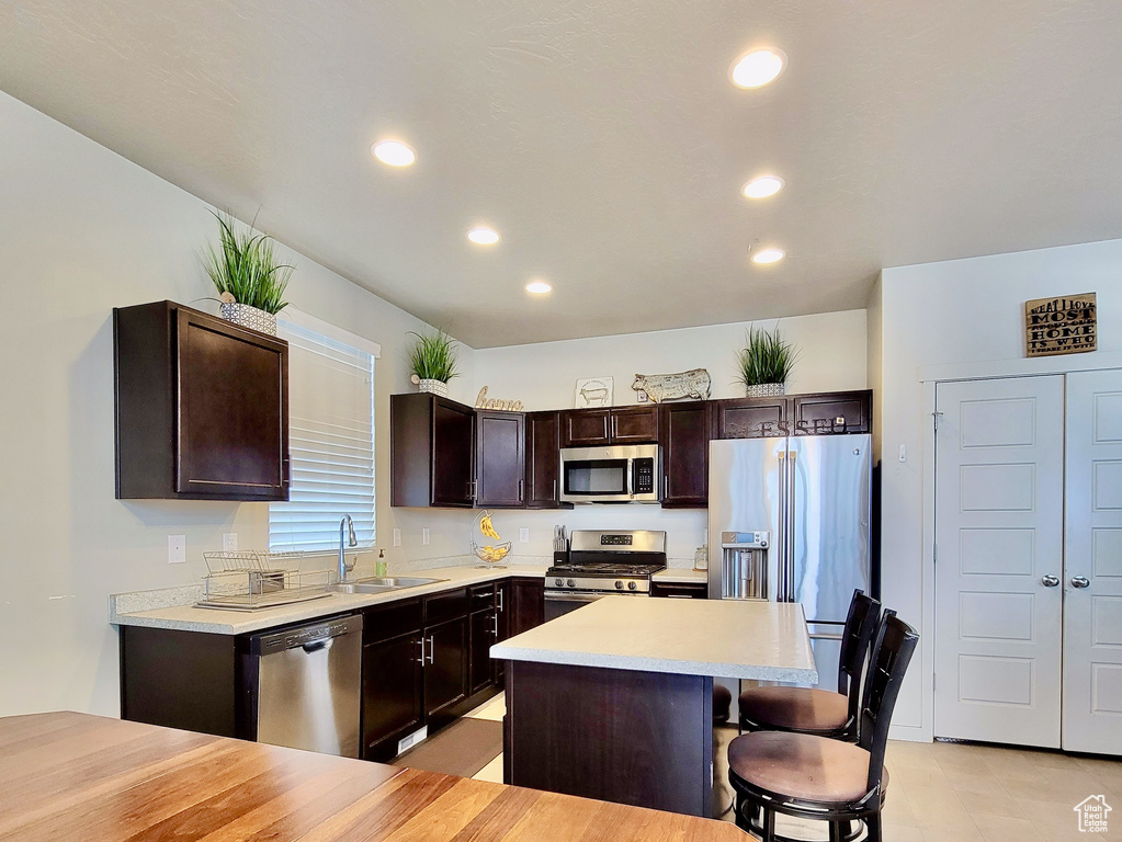 Kitchen with dark brown cabinetry, stainless steel appliances, a sink, and light countertops